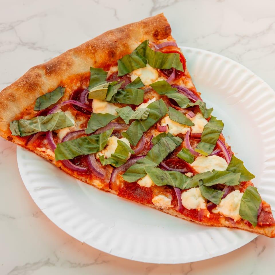Square pizza topped with melted cheese, red onions, tomato sauce, pepperoni, and fresh basil on a white plate.