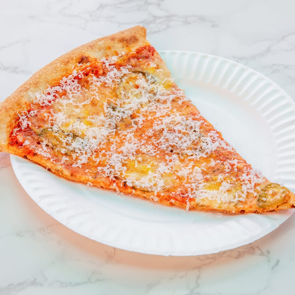 Triangular slice of cheesy pizza topped with tomato sauce and herbs on a white plate over marble.