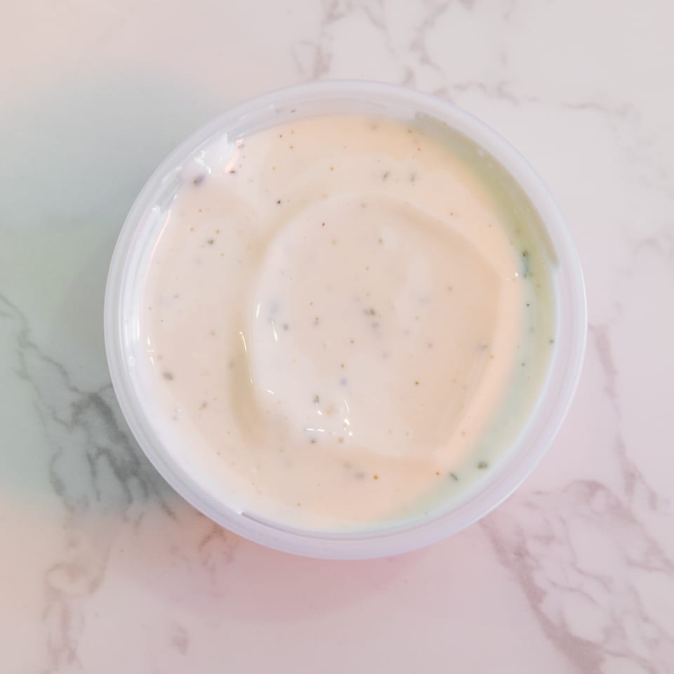 Small container of creamy herb-speckled dipping sauce on a marble countertop.