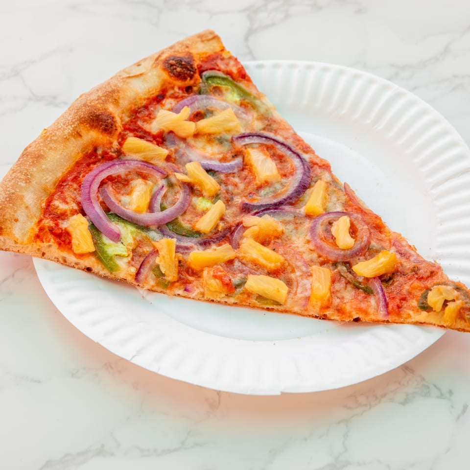 A slice of pineapple, red onion, green pepper, and cheese pizza on a white plate atop a marble surface.