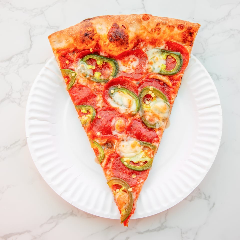 Triangular slice of pepperoni and jalapeño pizza on a white plate atop a marble surface.