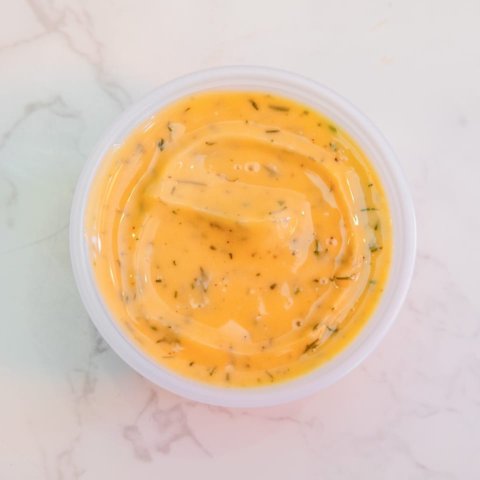 Round container of creamy orange herb-speckled dipping sauce on a white marble surface.