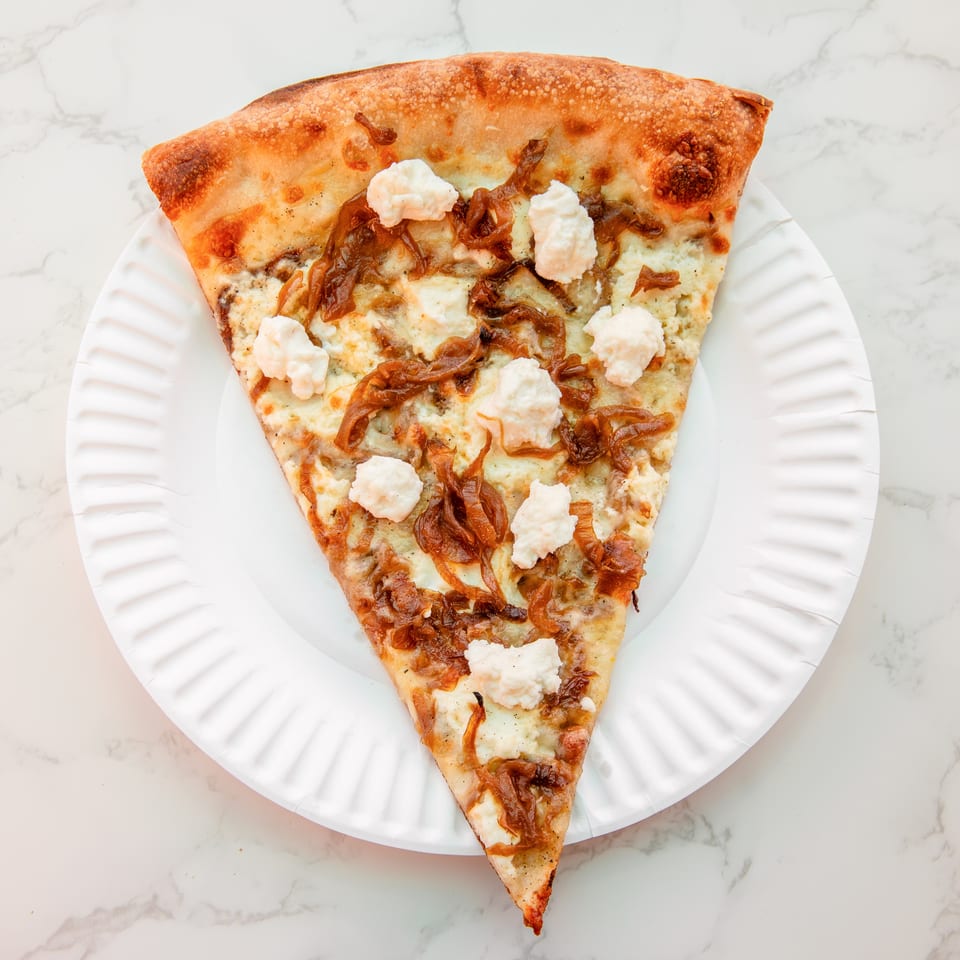 Triangular pizza slice topped with melted cheese, caramelized onions, and dollops of ricotta on a white plate.