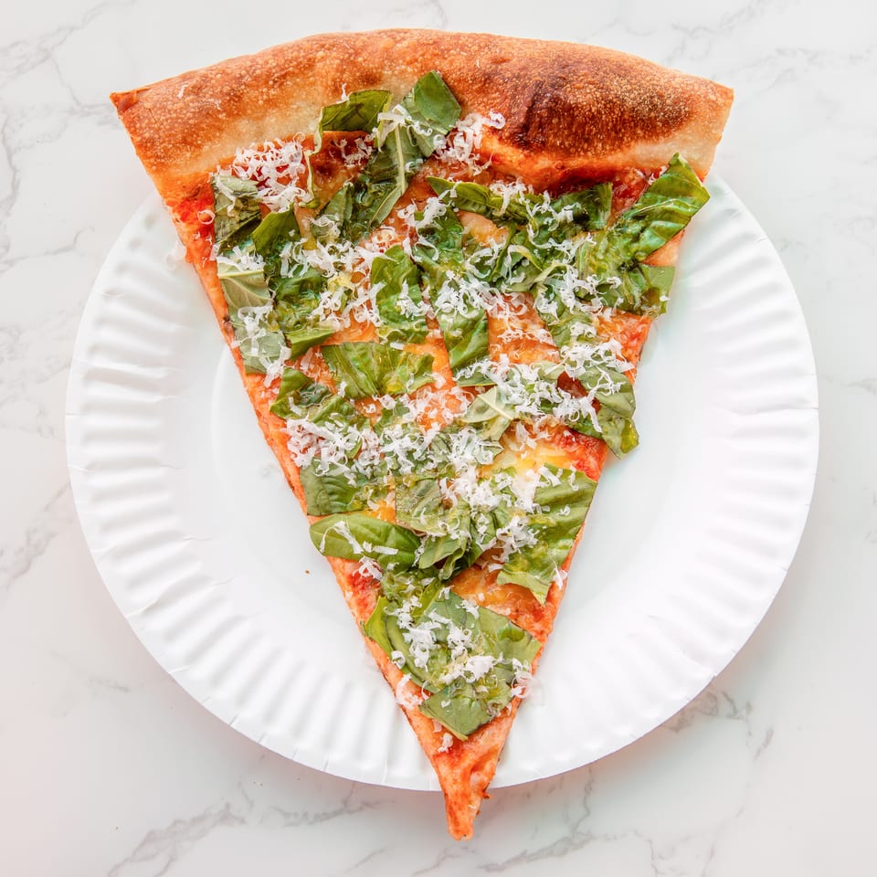 Overhead view of a rectangular pizza slice topped with fresh basil, tomato sauce, melted cheese, and grated cheese on a white plate.