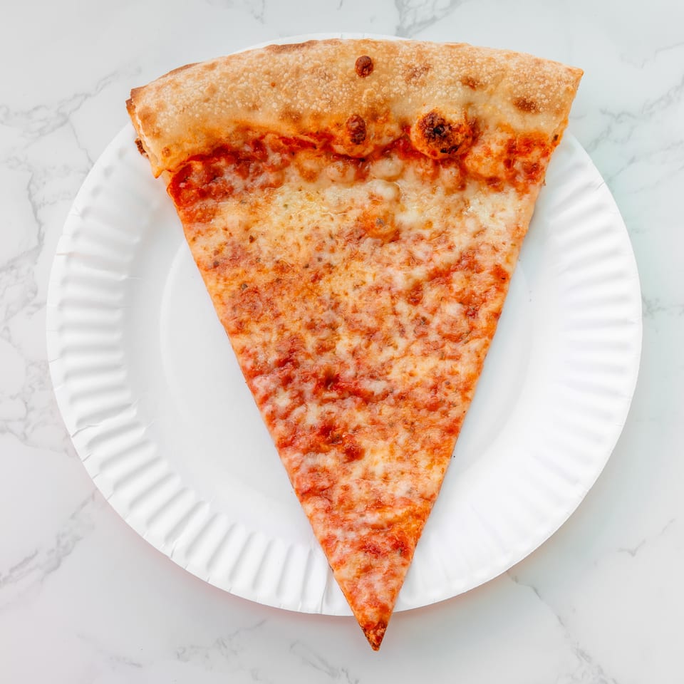 Large triangular cheese pizza slice with tomato sauce and browned toppings on a white paper plate.