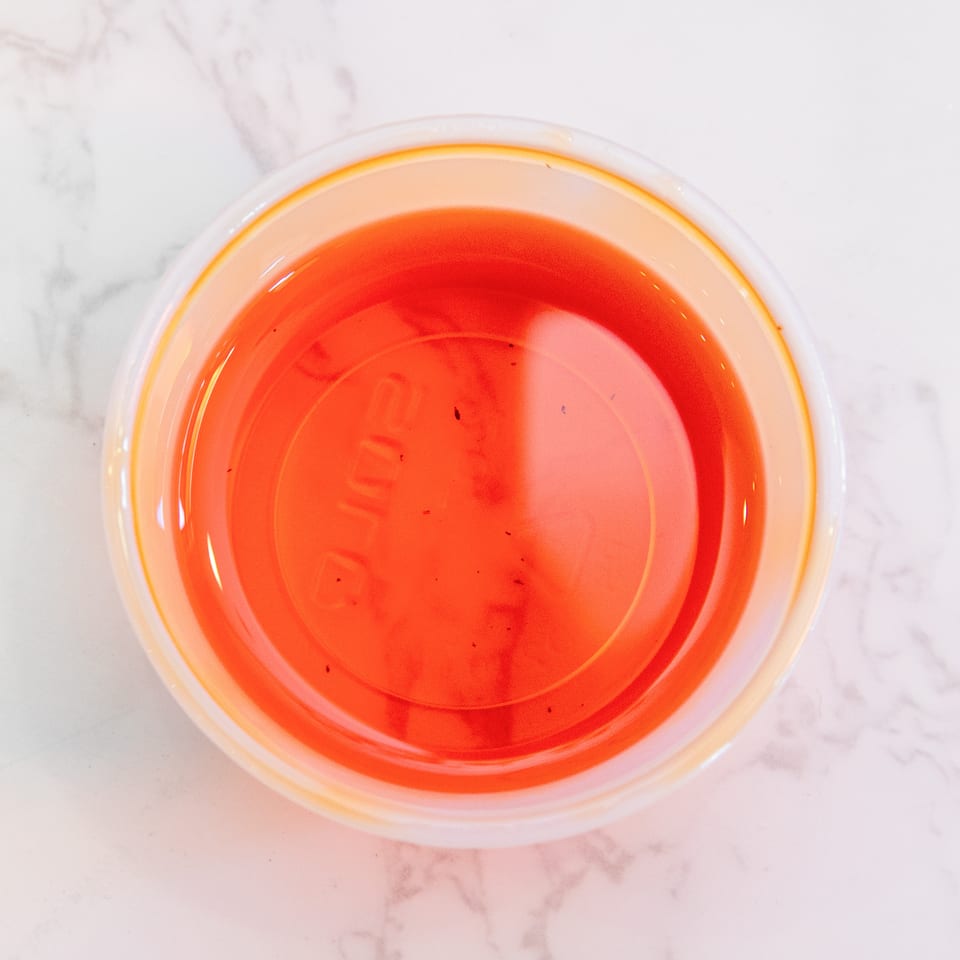 Overhead view of a glass filled with bright red-orange beverage on a white marble surface.