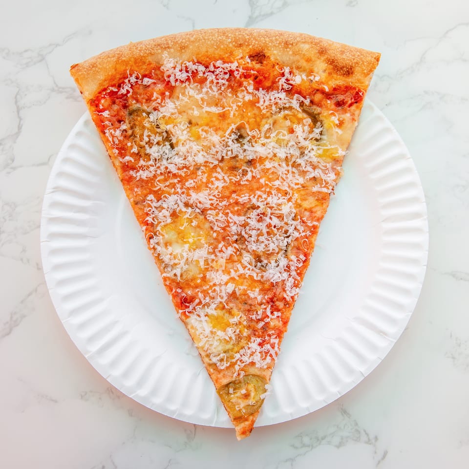 Triangular cheese pizza slice topped with tomato sauce, herbs, and grated cheese on a white plate.