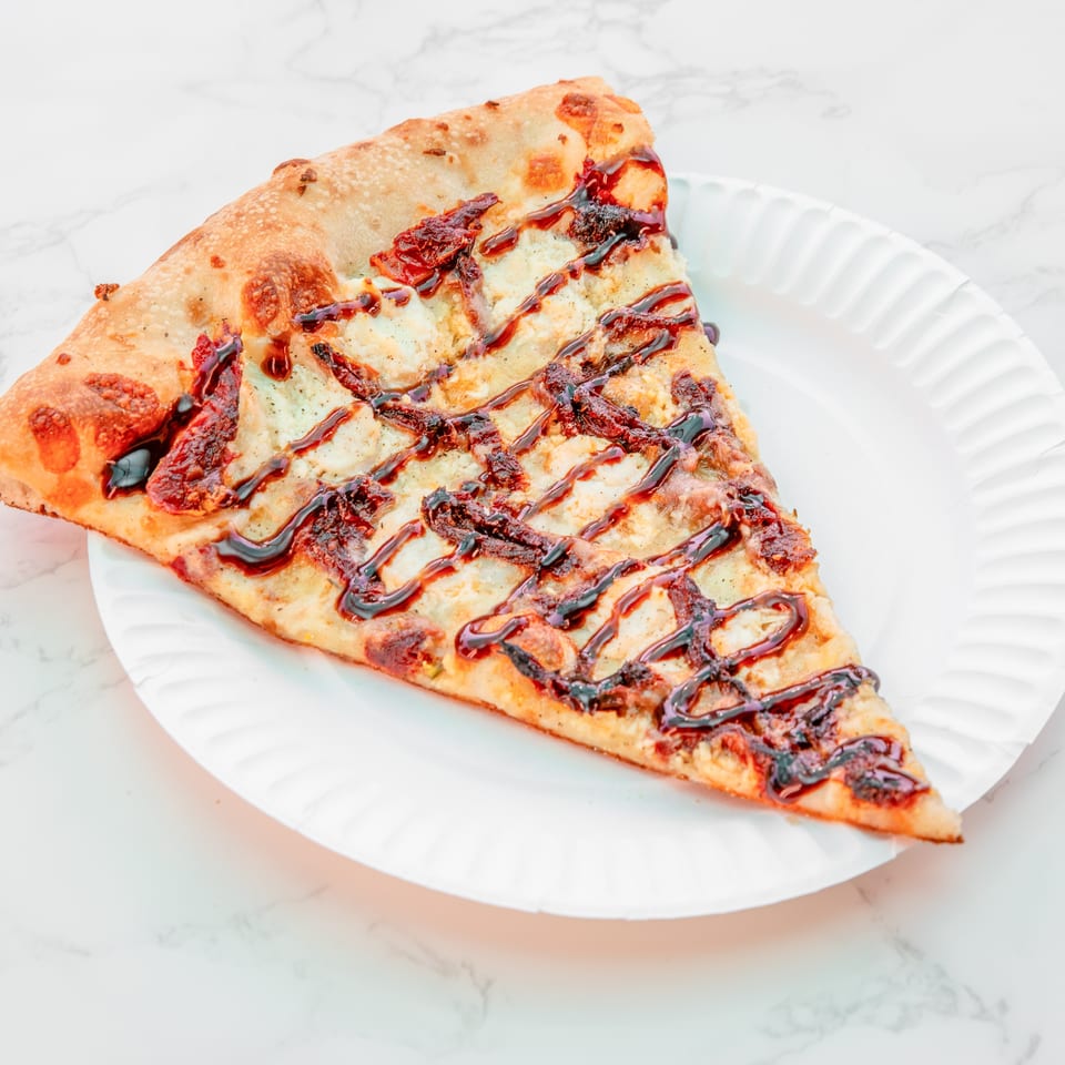 Triangular flatbread topped with melted cheese, sun-dried tomatoes, and balsamic drizzle on a white ridged plate.
